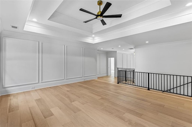 empty room with ceiling fan, a raised ceiling, a decorative wall, light wood-style flooring, and recessed lighting