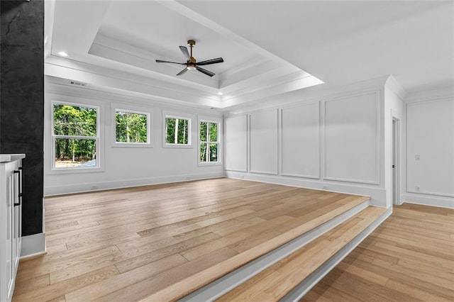 unfurnished living room featuring a decorative wall, ornamental molding, a ceiling fan, and light wood finished floors