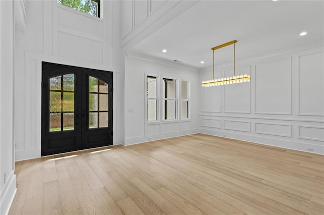 entrance foyer with ornamental molding, a decorative wall, recessed lighting, light wood-type flooring, and french doors
