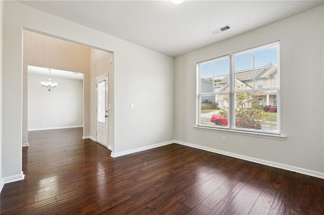 spare room featuring dark wood-type flooring, an inviting chandelier, and plenty of natural light