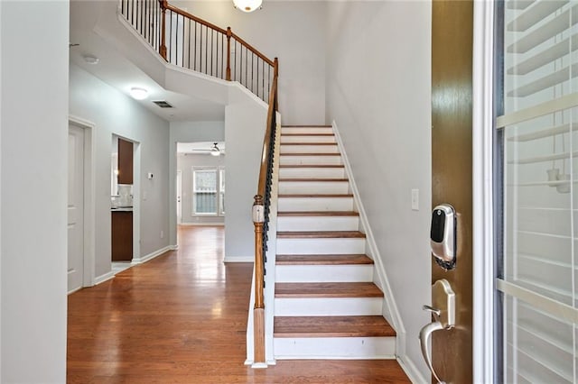 staircase featuring ceiling fan, wood-type flooring, and a high ceiling