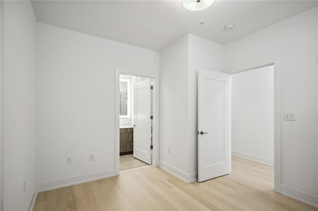 unfurnished bedroom featuring light wood-type flooring, baseboards, and ensuite bathroom