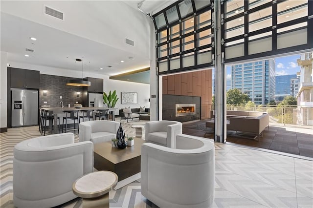 living area featuring a high ceiling, a view of city, visible vents, and a glass covered fireplace