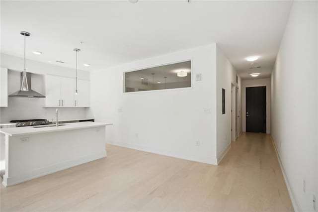 kitchen featuring a sink, white cabinetry, light countertops, wall chimney range hood, and light wood finished floors