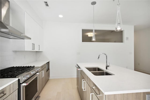 kitchen with stainless steel appliances, light countertops, a sink, wall chimney range hood, and modern cabinets