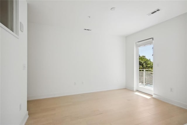 empty room with light wood finished floors, visible vents, and baseboards