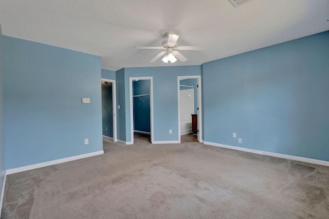 unfurnished bedroom featuring a walk in closet, a textured ceiling, carpet, baseboards, and a closet