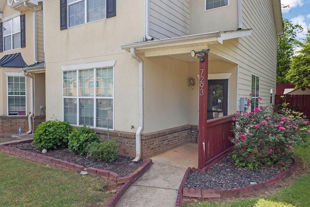doorway to property with covered porch, brick siding, and stucco siding