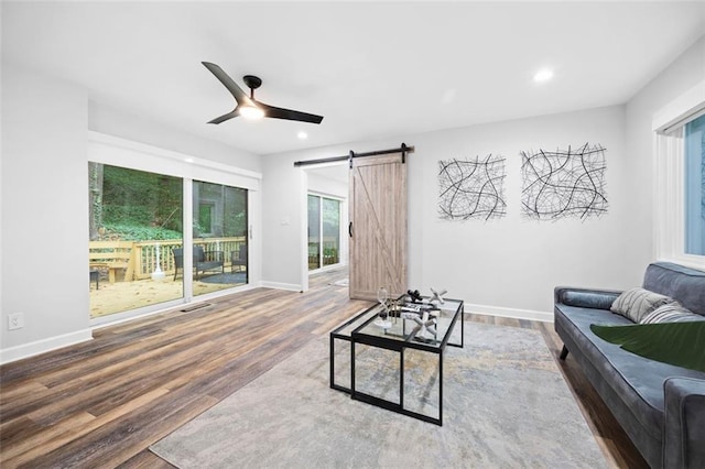 living room with ceiling fan, wood-type flooring, and a barn door