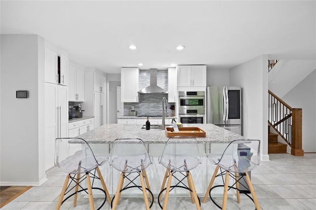 kitchen with a breakfast bar, light stone countertops, wall chimney range hood, and appliances with stainless steel finishes