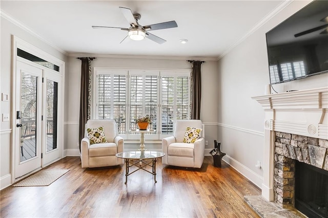 sitting room featuring ceiling fan, a stone fireplace, wood finished floors, and crown molding