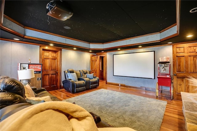 home theater with recessed lighting, ornamental molding, a raised ceiling, and wood finished floors