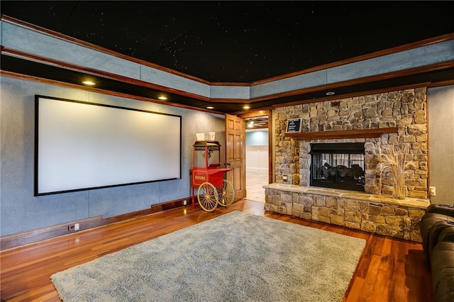 home theater room featuring a fireplace, a tray ceiling, wood finished floors, and ornamental molding