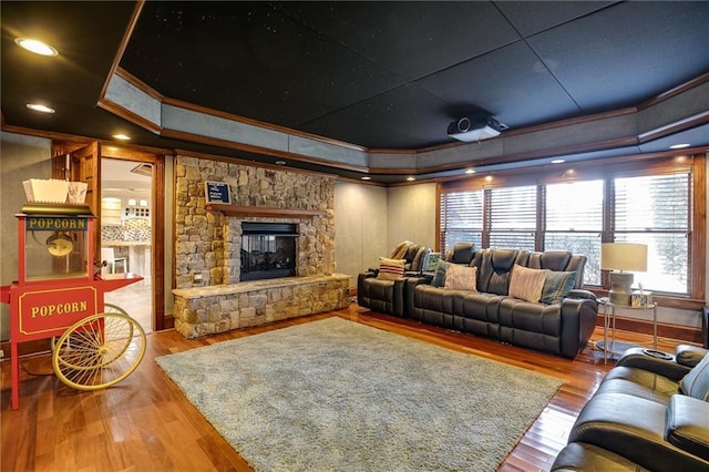 living area featuring a fireplace, a raised ceiling, wood finished floors, and ornamental molding