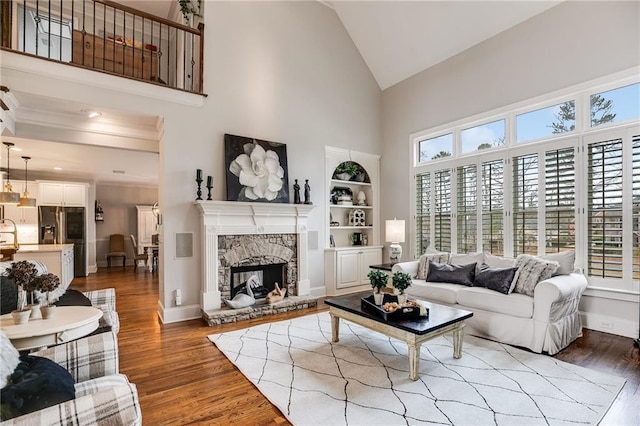 living area with baseboards, high vaulted ceiling, a stone fireplace, and wood finished floors