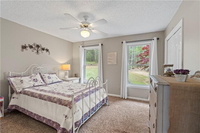 bedroom with a textured ceiling, light colored carpet, multiple windows, and ceiling fan