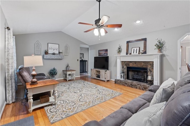 living room featuring hardwood / wood-style flooring, ceiling fan, a stone fireplace, and lofted ceiling