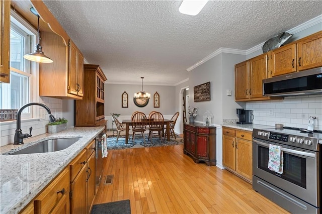 kitchen with sink, light wood-type flooring, ornamental molding, appliances with stainless steel finishes, and decorative light fixtures