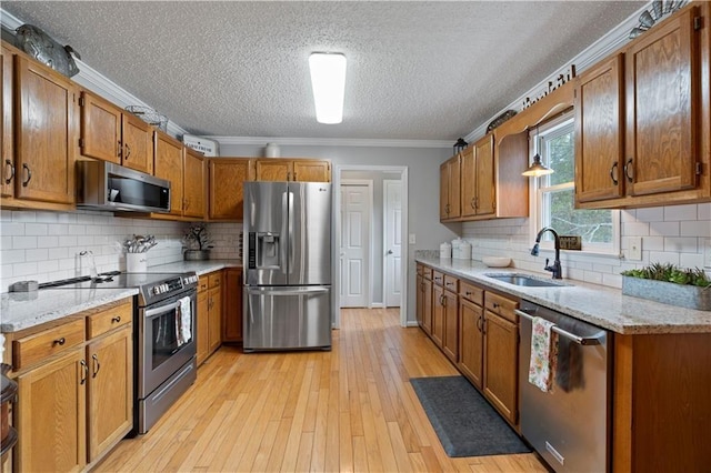 kitchen featuring sink, light hardwood / wood-style flooring, backsplash, crown molding, and appliances with stainless steel finishes