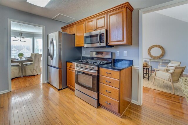 kitchen with a chandelier, light wood-type flooring, a textured ceiling, and appliances with stainless steel finishes