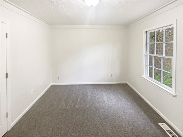 empty room with baseboards, visible vents, dark colored carpet, a textured ceiling, and crown molding