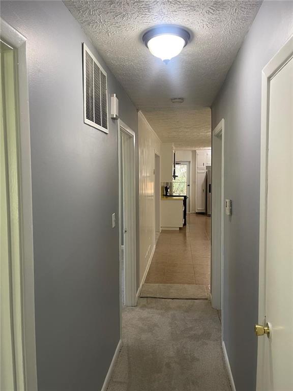 hallway with a textured ceiling and light colored carpet