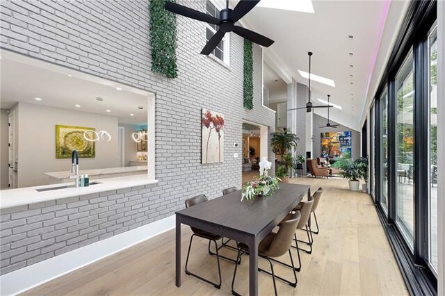 dining area with light hardwood / wood-style flooring, high vaulted ceiling, ceiling fan, and brick wall