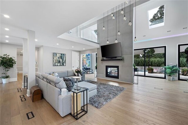 living room with a large fireplace, light hardwood / wood-style flooring, and a towering ceiling