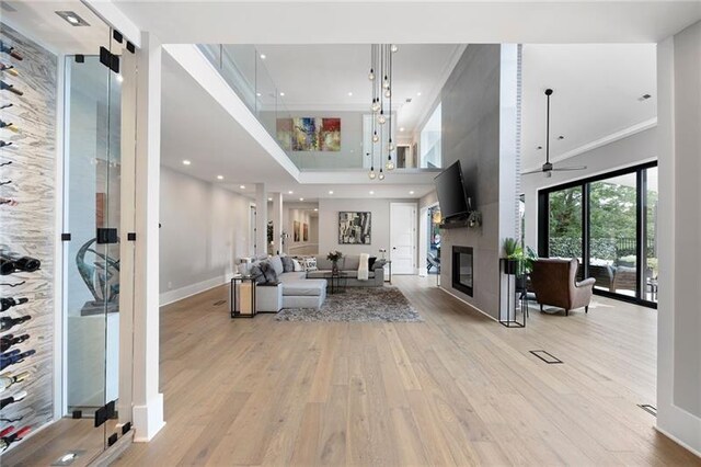 living room featuring ceiling fan, a high ceiling, light hardwood / wood-style flooring, a fireplace, and ornamental molding