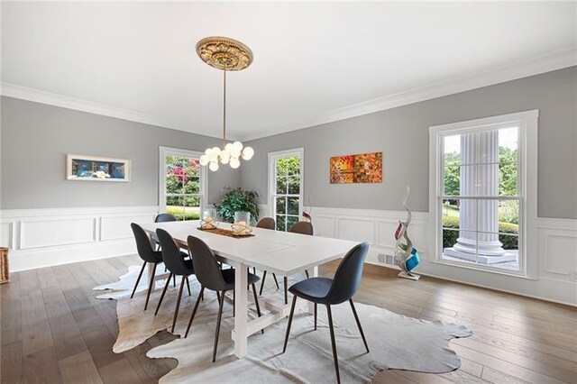 dining area with hardwood / wood-style floors, ornamental molding, and an inviting chandelier