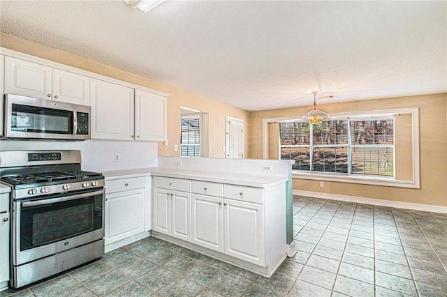 kitchen with appliances with stainless steel finishes, a peninsula, light countertops, white cabinetry, and pendant lighting