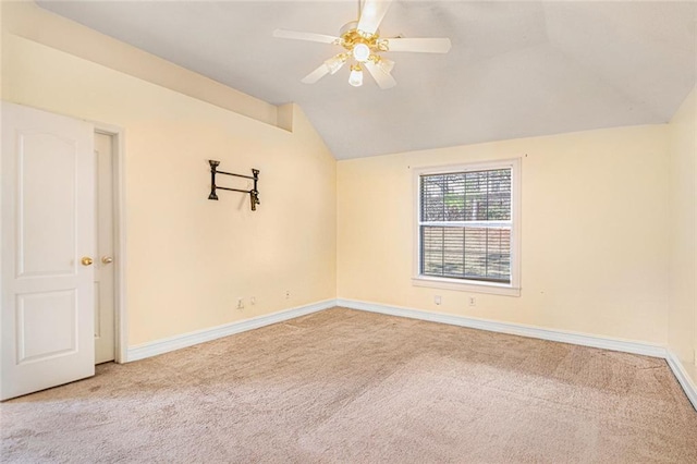 spare room with a ceiling fan, lofted ceiling, light colored carpet, and baseboards