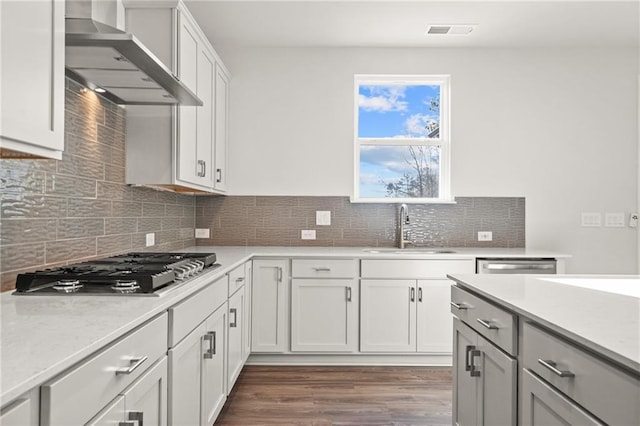 kitchen with appliances with stainless steel finishes, sink, white cabinets, dark wood-type flooring, and wall chimney range hood