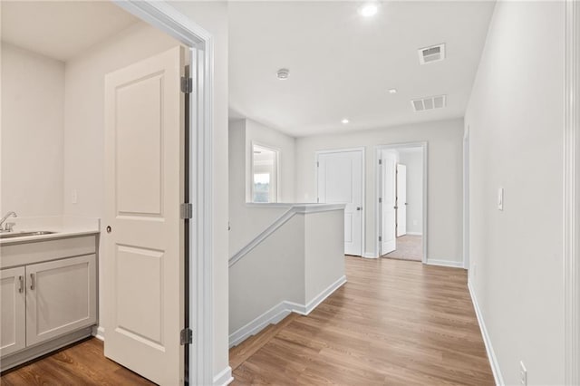 corridor with light hardwood / wood-style floors and sink