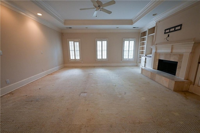 unfurnished living room featuring ceiling fan, a tiled fireplace, crown molding, and a tray ceiling