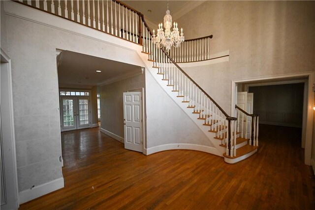 staircase featuring french doors, crown molding, a towering ceiling, wood-type flooring, and a chandelier
