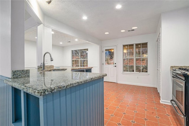 kitchen with gas stove, sink, stone countertops, a textured ceiling, and kitchen peninsula