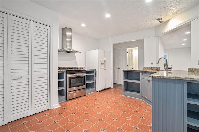 kitchen with sink, gas range, a textured ceiling, white fridge with ice dispenser, and wall chimney range hood