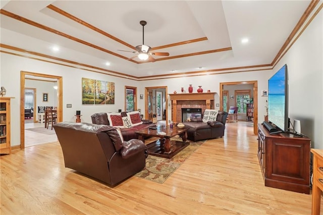 169 Robson Trl, Mcdonough, GA 30252 - living area featuring a raised ceiling, ceiling fan, crown molding, light wood-type flooring, and a glass covered fireplace