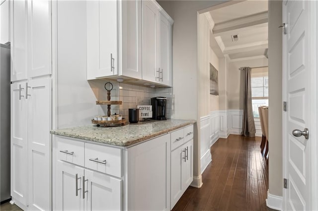 kitchen with white cabinets, a wainscoted wall, light stone counters, ornamental molding, and dark wood-style flooring