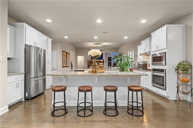 kitchen with white cabinets, dark wood-style floors, appliances with stainless steel finishes, a kitchen breakfast bar, and light stone countertops