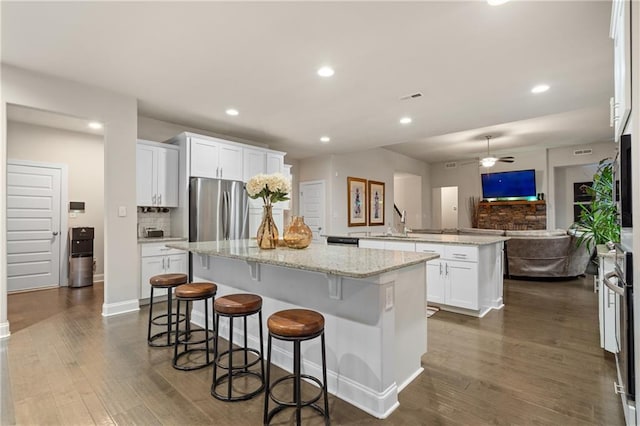 kitchen featuring a kitchen island, light stone counters, open floor plan, freestanding refrigerator, and white cabinetry