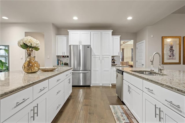 kitchen with dark wood finished floors, white cabinets, light stone counters, appliances with stainless steel finishes, and a sink