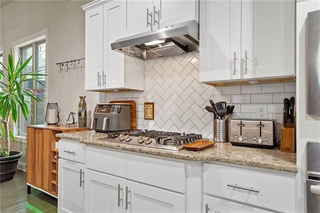 kitchen featuring light stone countertops, under cabinet range hood, white cabinetry, decorative backsplash, and stainless steel gas stovetop