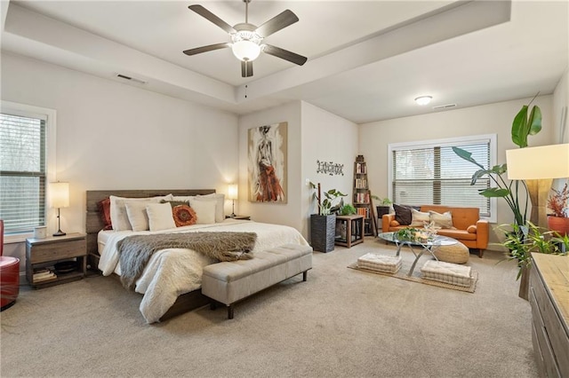 bedroom featuring a tray ceiling, a ceiling fan, visible vents, and light colored carpet