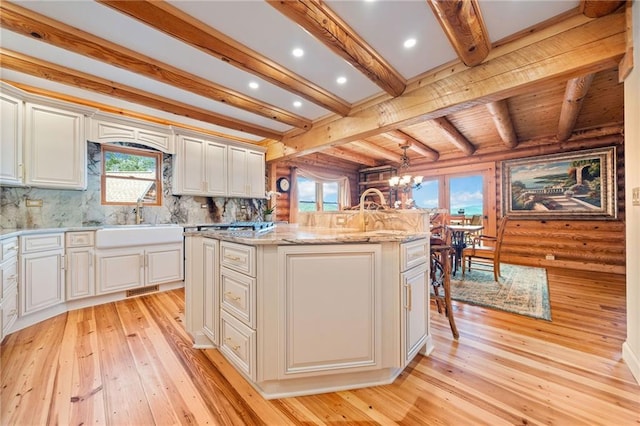 kitchen with beamed ceiling, a kitchen island with sink, light hardwood / wood-style flooring, sink, and white cabinets