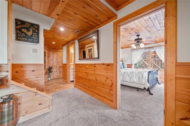 hallway featuring light carpet, wooden walls, and wood ceiling