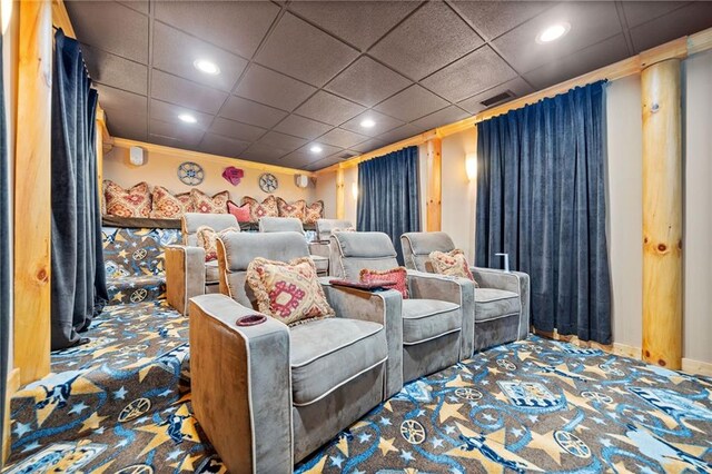 carpeted home theater room featuring a drop ceiling and crown molding