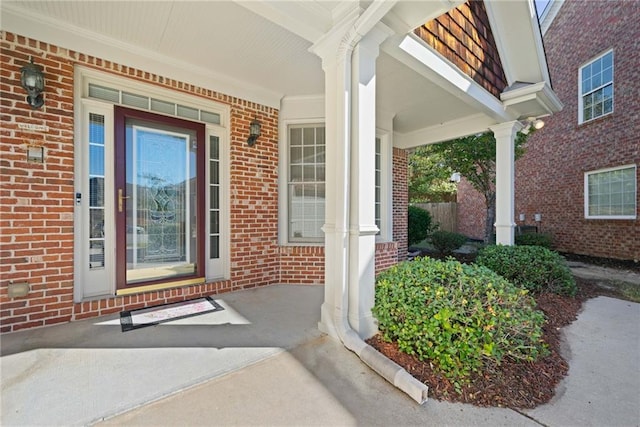 view of exterior entry with brick siding and a porch