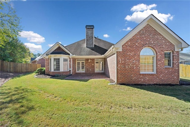 back of house featuring brick siding, fence, french doors, a chimney, and a yard